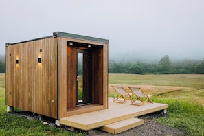 A wooden cabin with a door, a small porch, and two chairs. - Otherland Hotel (Newfane)