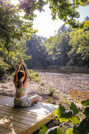 A person performing yoga on a wooden deck overlooking a river with trees in the background.