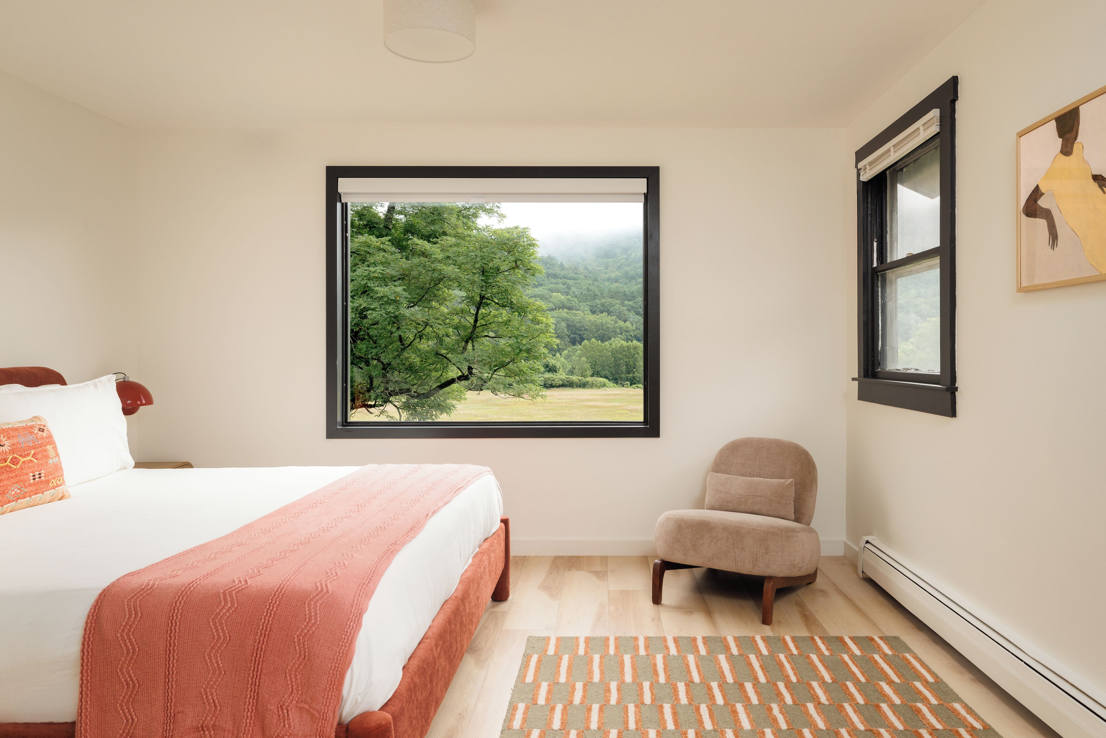 Een slaapkamer met een groot bed, een stoel, een raam met uitzicht op bomen en een radiator.