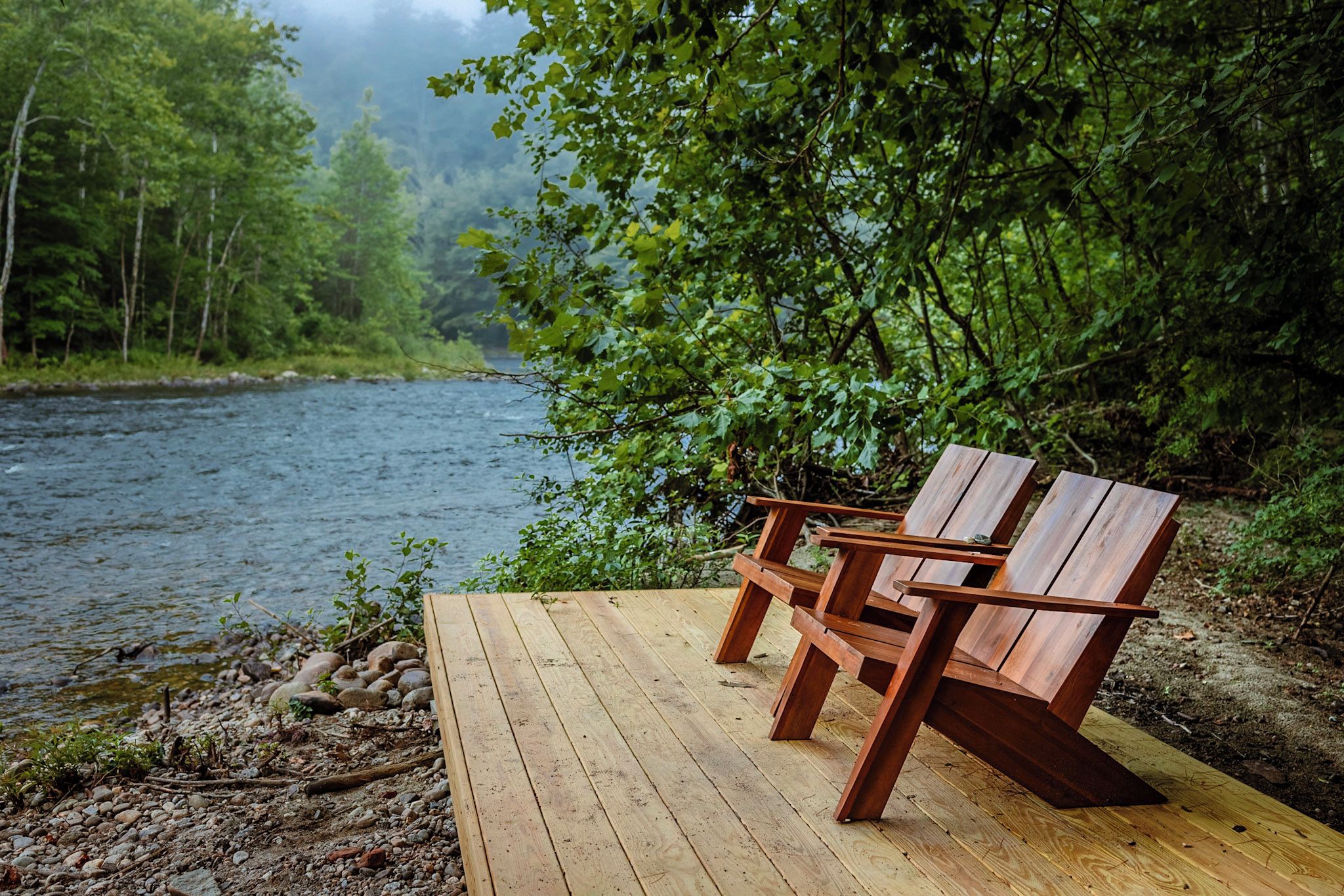 Un banco de madera junto a un río, con un bosque de fondo.