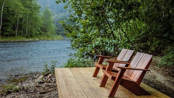 Un banco de madera junto a un río, con un bosque de fondo.