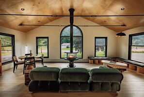 Amplia habitación con techo alto, chimenea y ventanas grandes que ofrecen vistas al exterior.