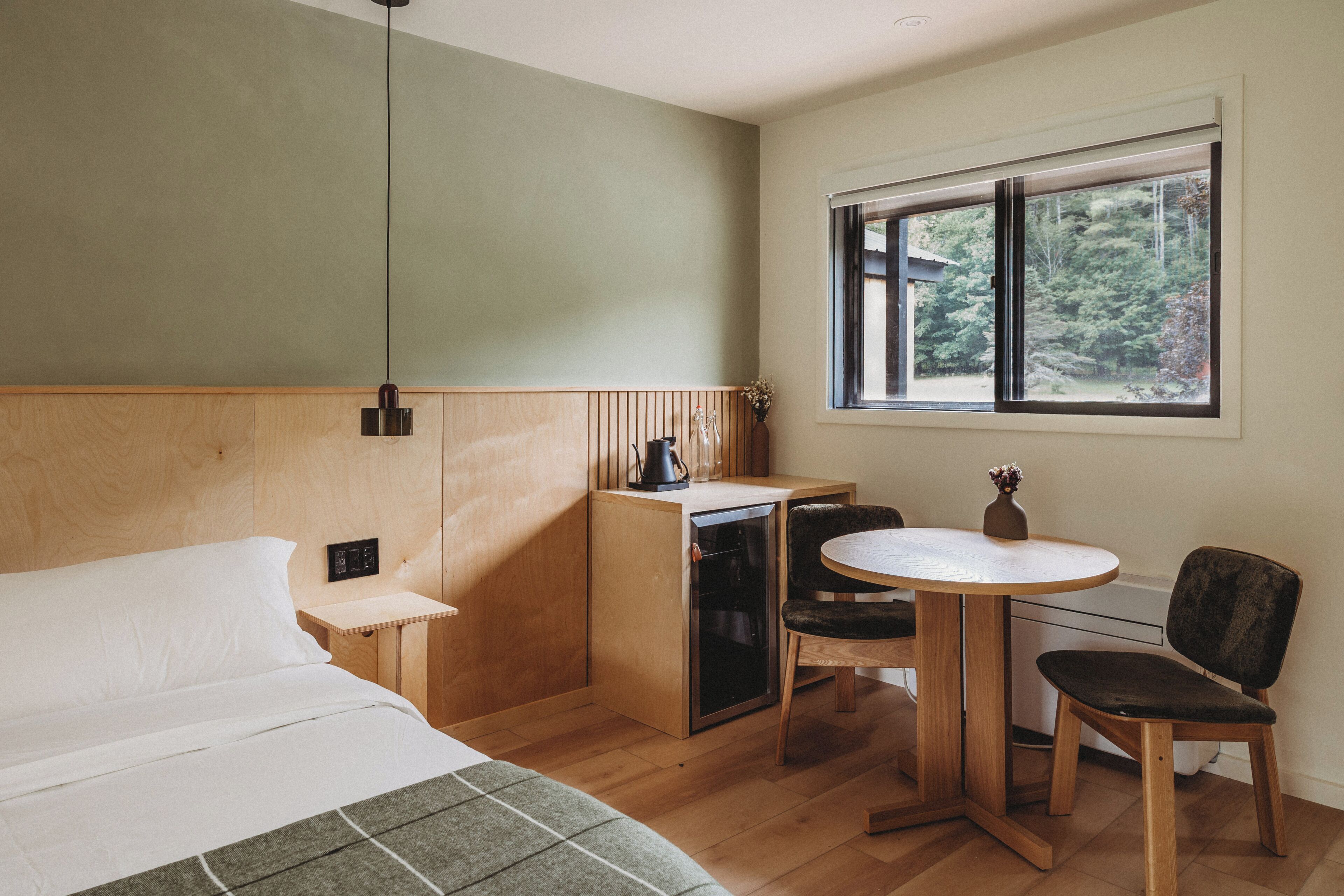 Habitación de hotel compacta con cama, un pequeño escritorio, una silla y ventana con vistas a zonas verdes.