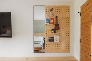 A bedroom with a bed, a wooden pegboard wall with books and a guitar, and a TV mounted on the wall.