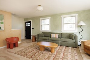 A living room with a sofa, a coffee table, a red chair, a lamp, and a patterned rug.