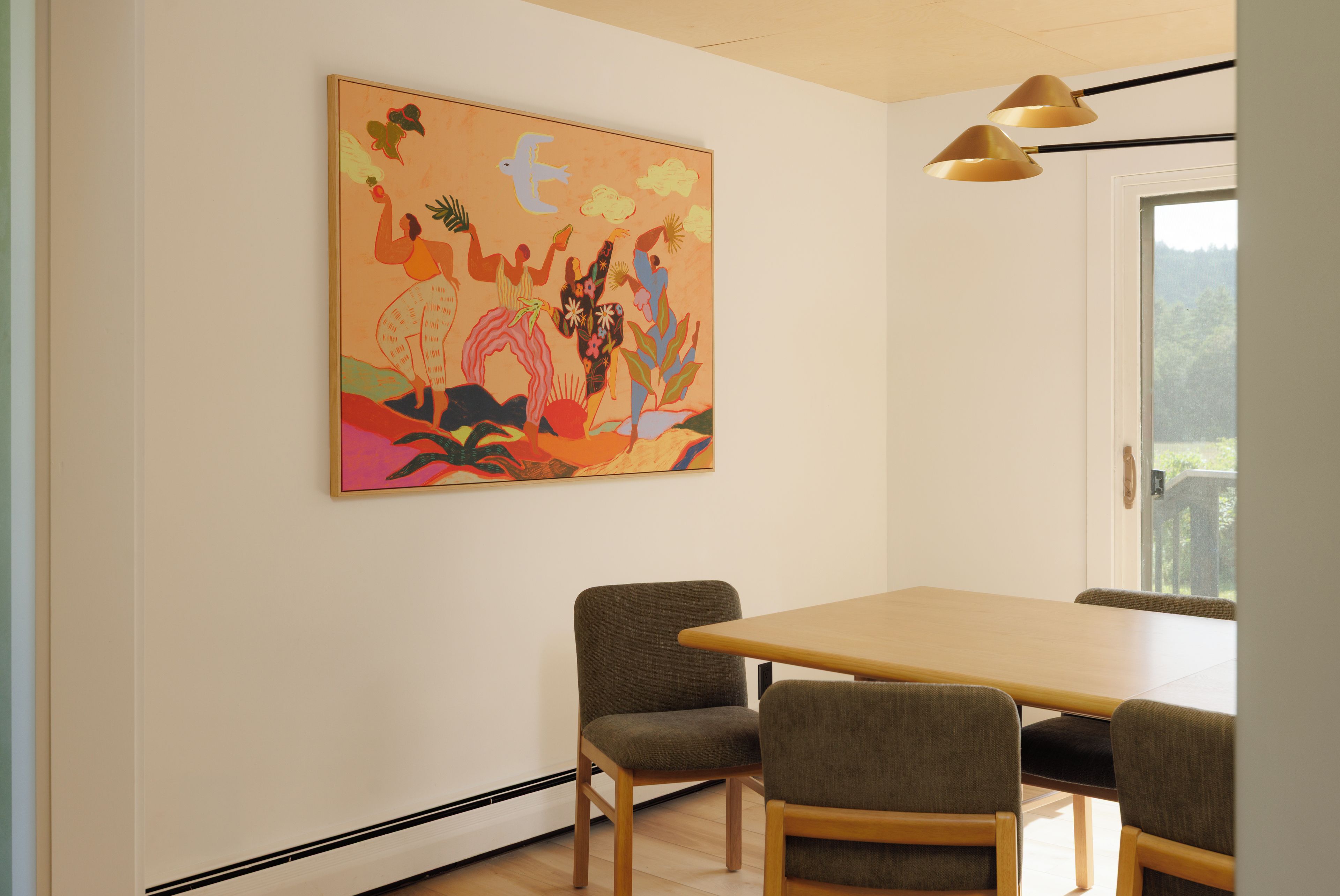 A dining area with a wooden table and four chairs, a colorful abstract painting on the wall, and a ceiling light fixture.