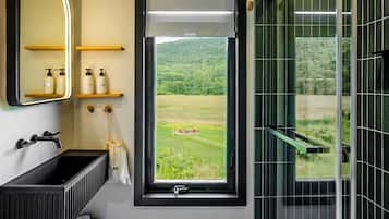 Ein modernes Badezimmer mit großem Fenster, einem schwarzen Waschbecken, einem Spiegel und einer Duschkabine aus Glas.