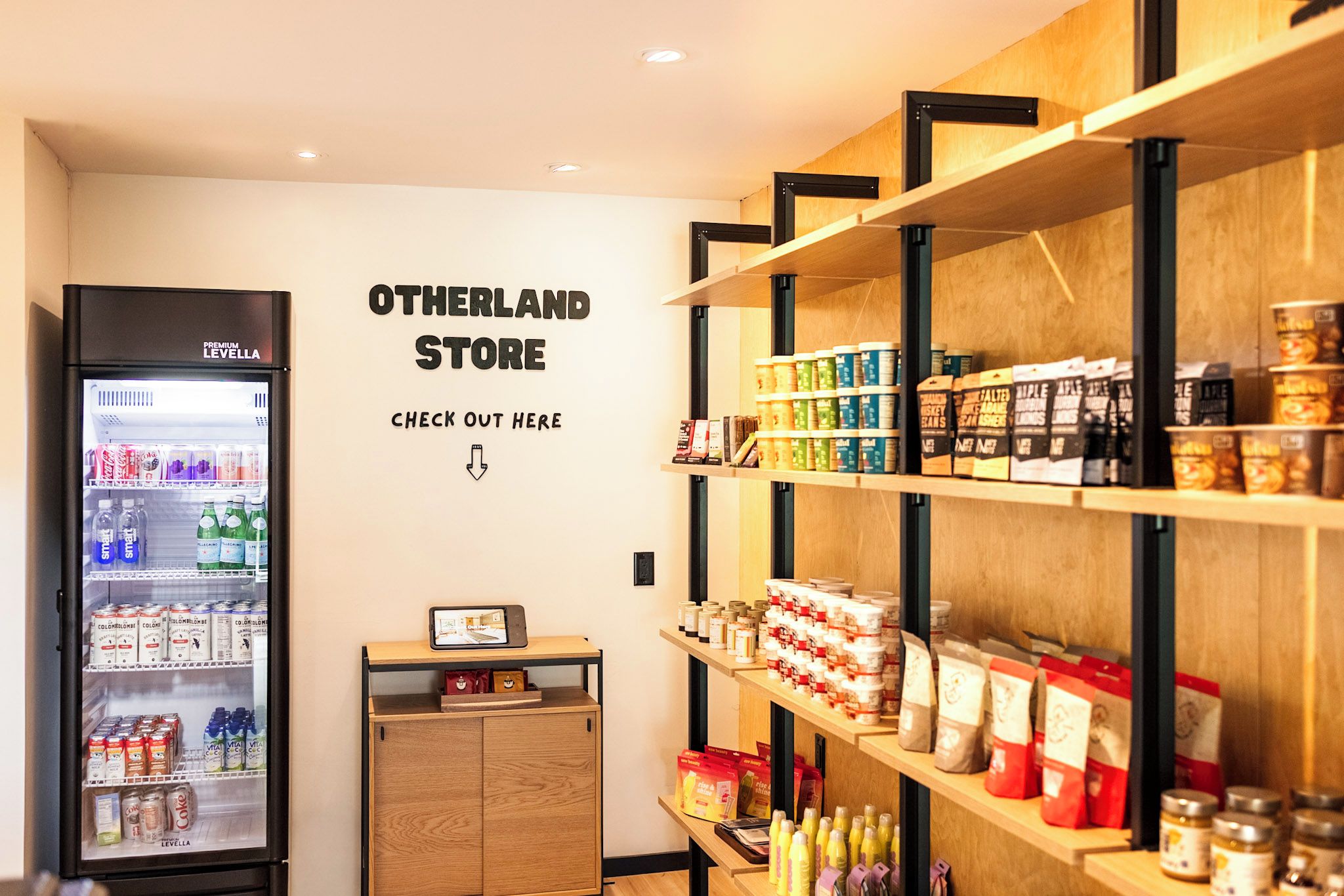 Interior de una tienda con estantes llenos de diversos productos, un refrigerador y un cartel en la pared.