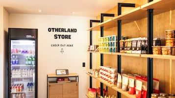 Interior de una tienda con estantes llenos de diversos productos, un refrigerador y un cartel en la pared.