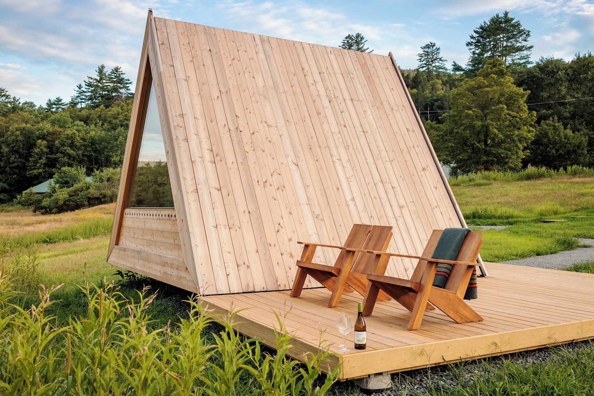 Une terrasse en bois avec une grande structure en bois inclinée, deux chaises en bois et une bouteille de vin.
