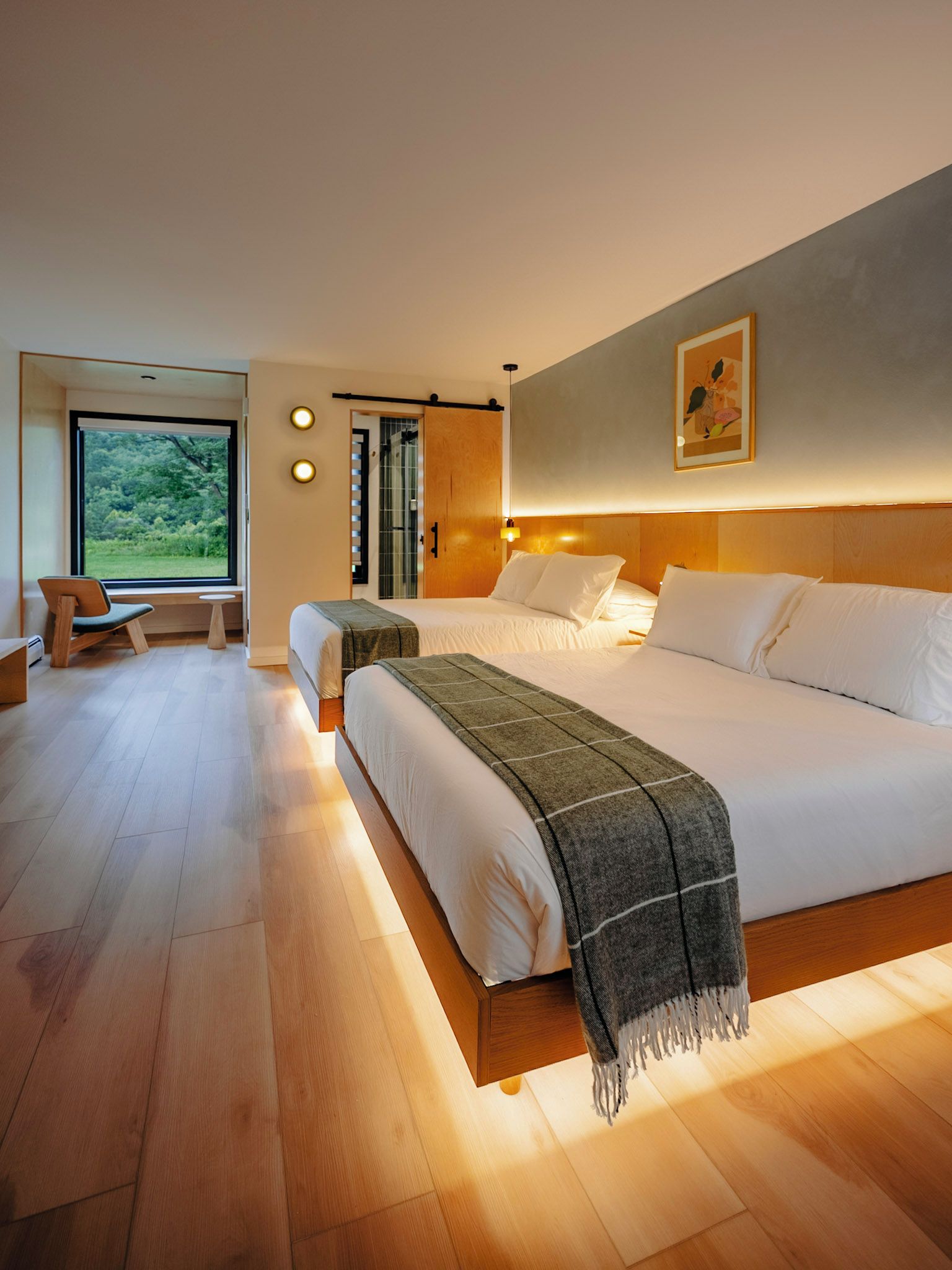 A modern hotel room with a large bed, two bedside tables, a bench, and a view of greenery.