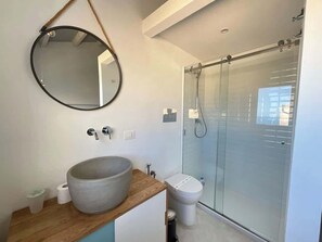 A modern bathroom with a round mirror, a large sink, a toilet, and a glass-enclosed shower.