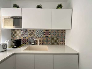 A compact kitchen with white cabinets, a stainless steel oven, a patterned backsplash, and a coffee maker.