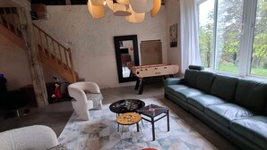 Una sala de estar con sofá, una mesa de centro, alfombra estampada, lámpara colgante y vista por una ventana.