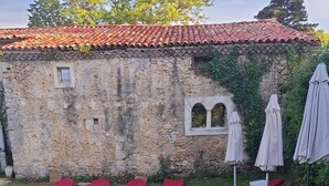 Una piscina con sillas de descanso rojas, un edificio de piedra con techo de tejas y sombrillas.