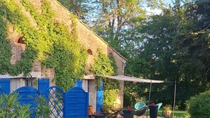 Una casa con techo inclinado, contraventanas azules y un jardín con césped y árboles.