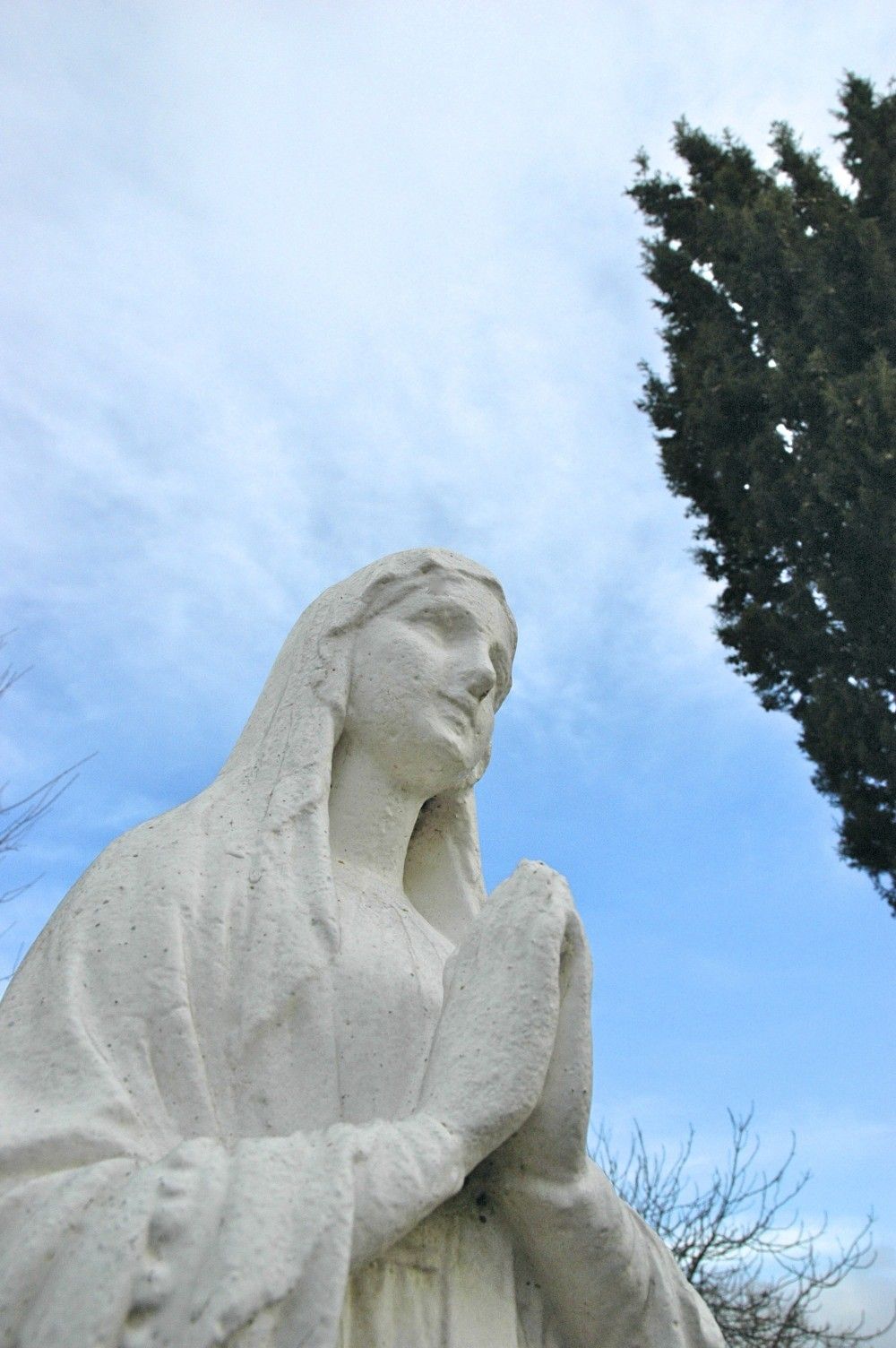 Une statue d’une femme vêtue d’une robe blanche, avec un arbre en arrière-plan.