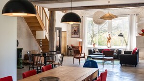 Un amplio espacio habitable con una mesa de comedor de madera, sillas rojas, un sofá negro y una escalera que sube a un nivel superior.