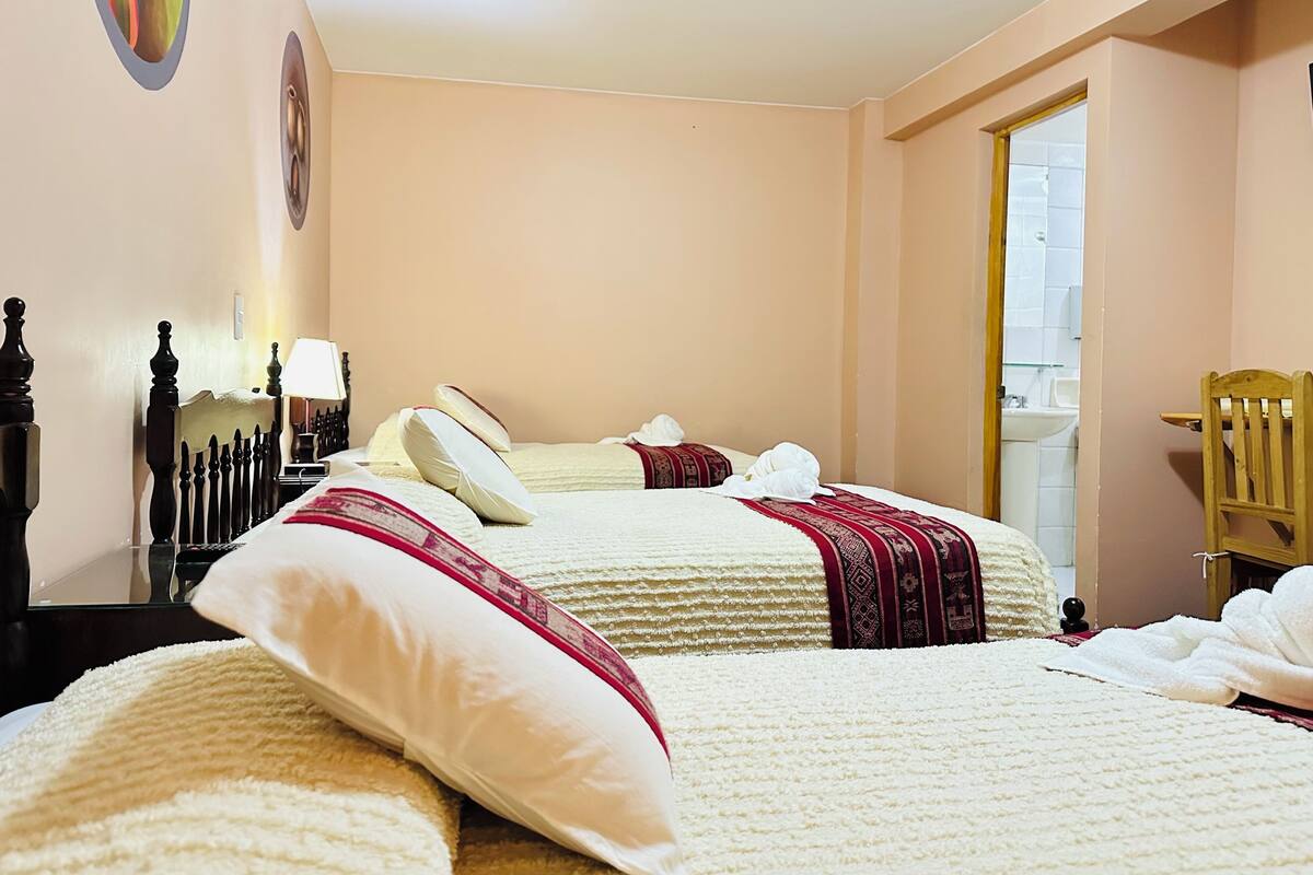 Een hotelkamer met twee bedden, een houten stoel, een nachtkastje met een lamp, en een badkamer die door een open deur zichtbaar is.