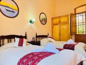 Een hotelkamer met twee bedden, een houten garderobe, een wandlamp en een raam met gordijnen.