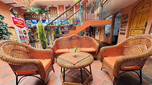 A cozy outdoor seating area with wicker furniture and a tiled floor, surrounded by a multi-level building with balconies and various signs.