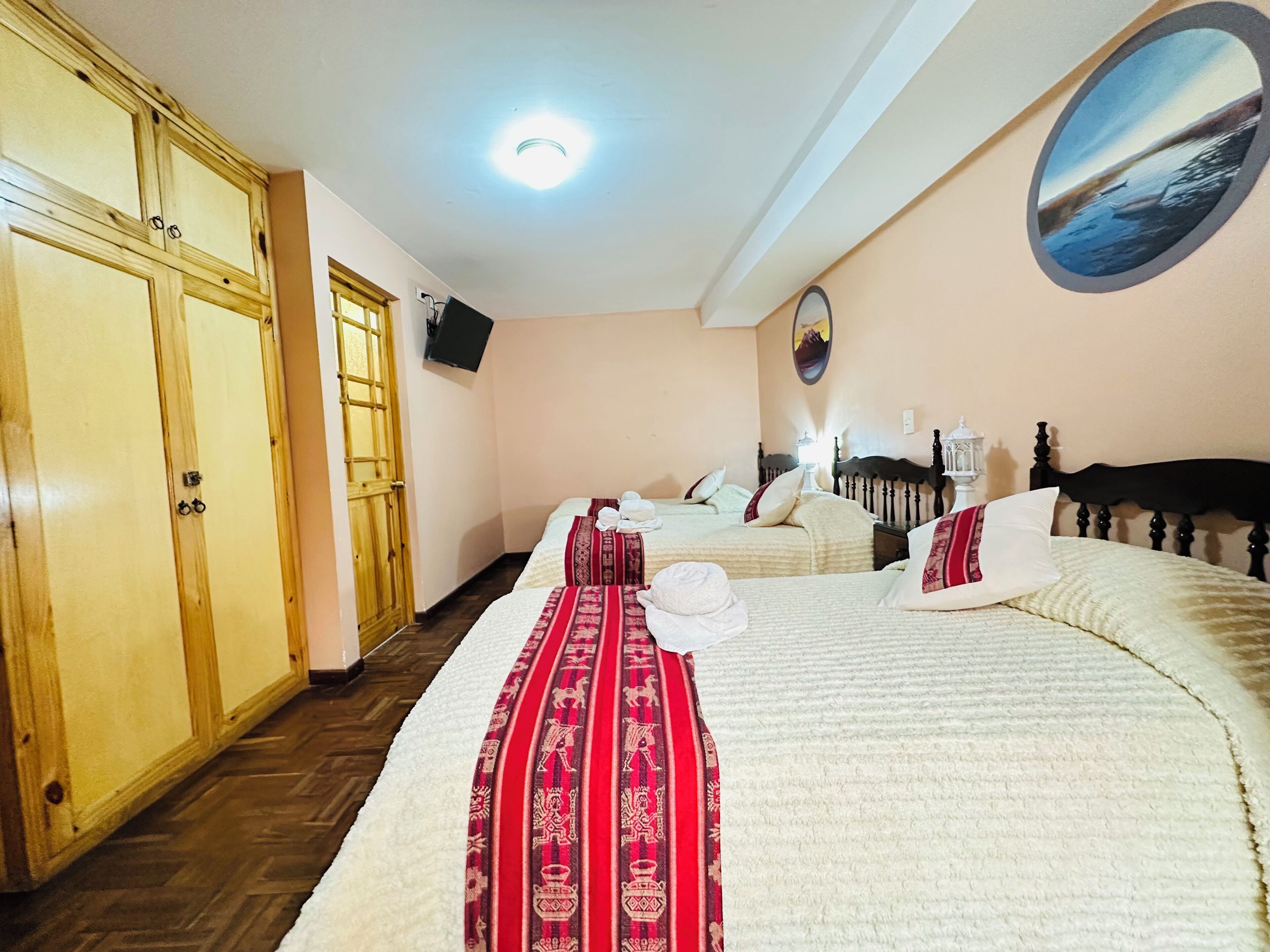 Habitación de hotel con dos camas, un armario de madera, un televisor y un cuadro en la pared.