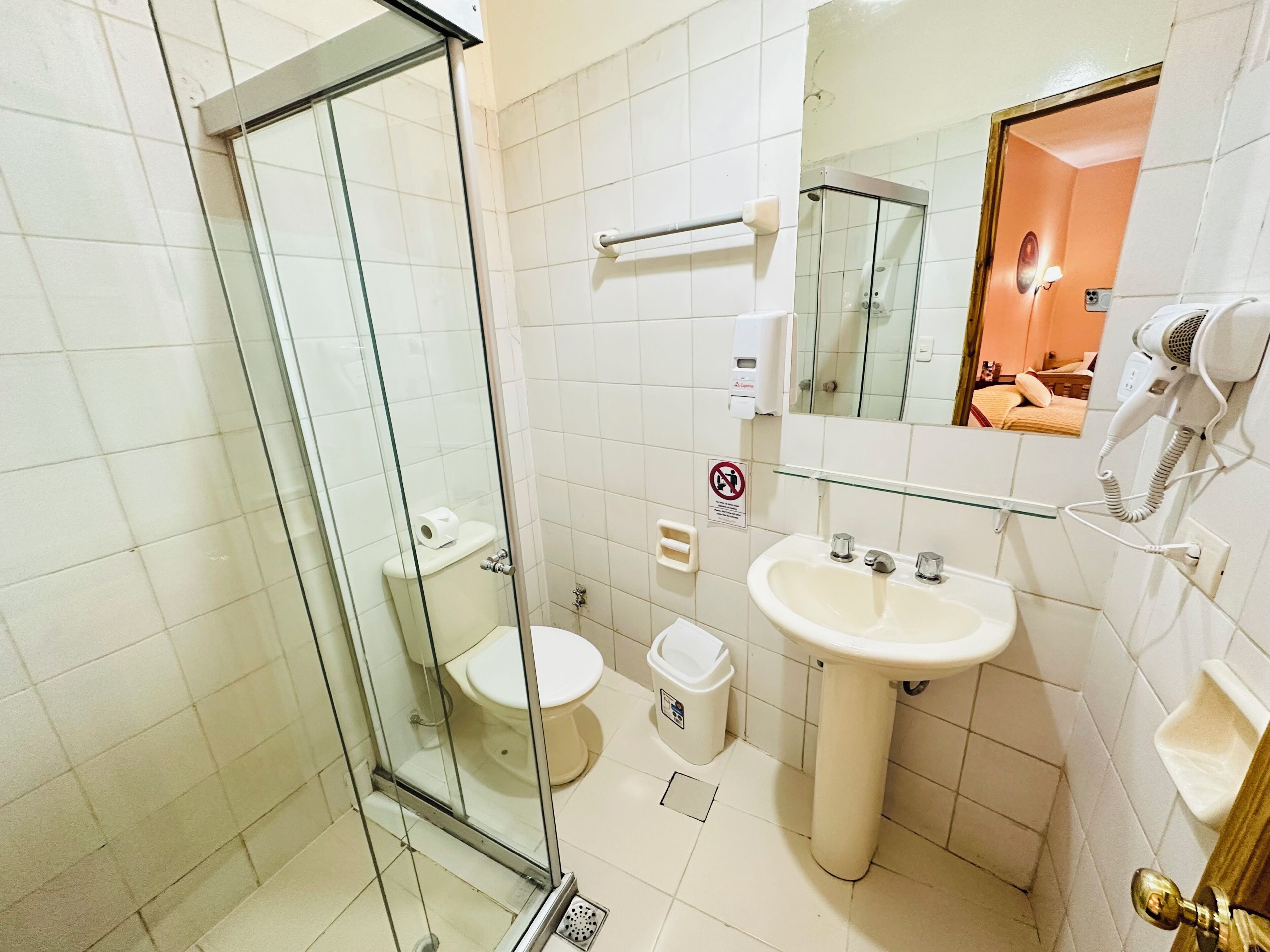 Baño con ducha envuelta en vidrio, inodoro, lavamanos y secador de pelo en la pared.