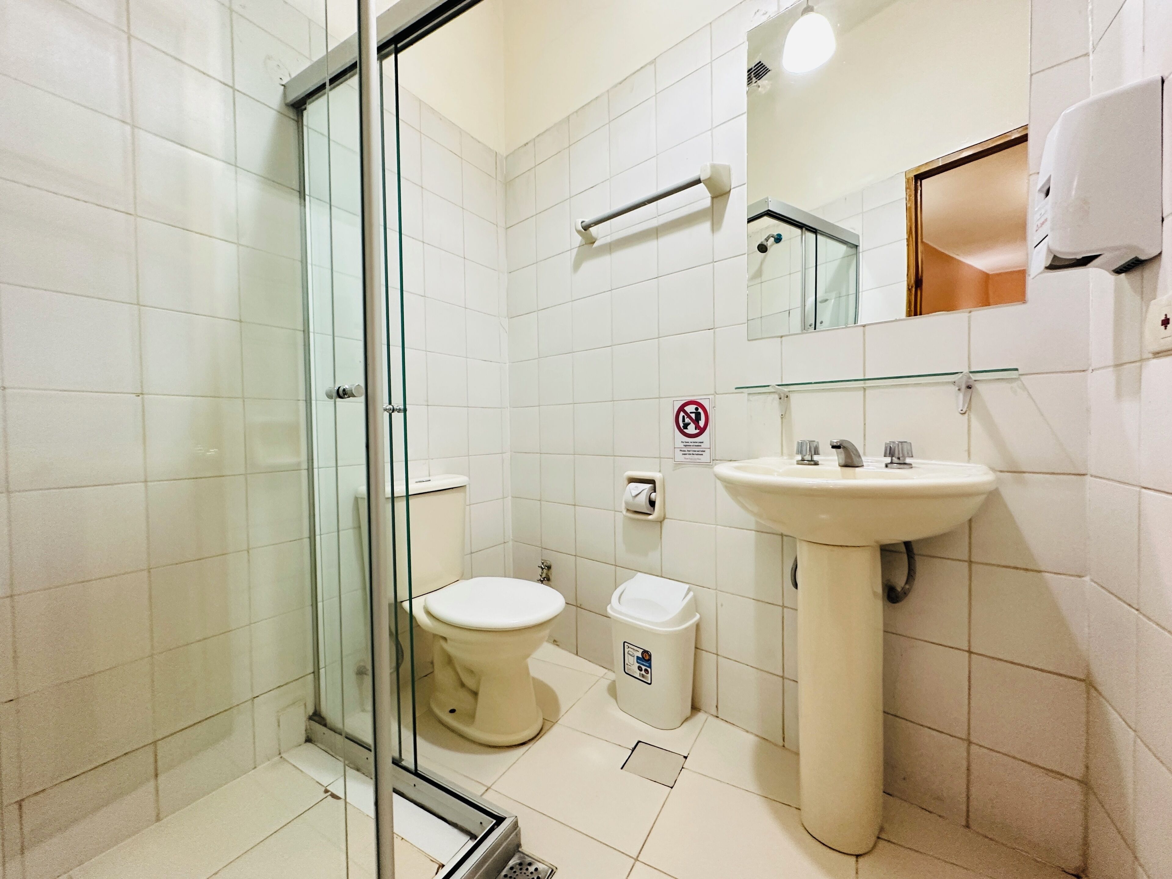 A bathroom with a glass shower enclosure, a toilet, a sink, and a hand dryer.