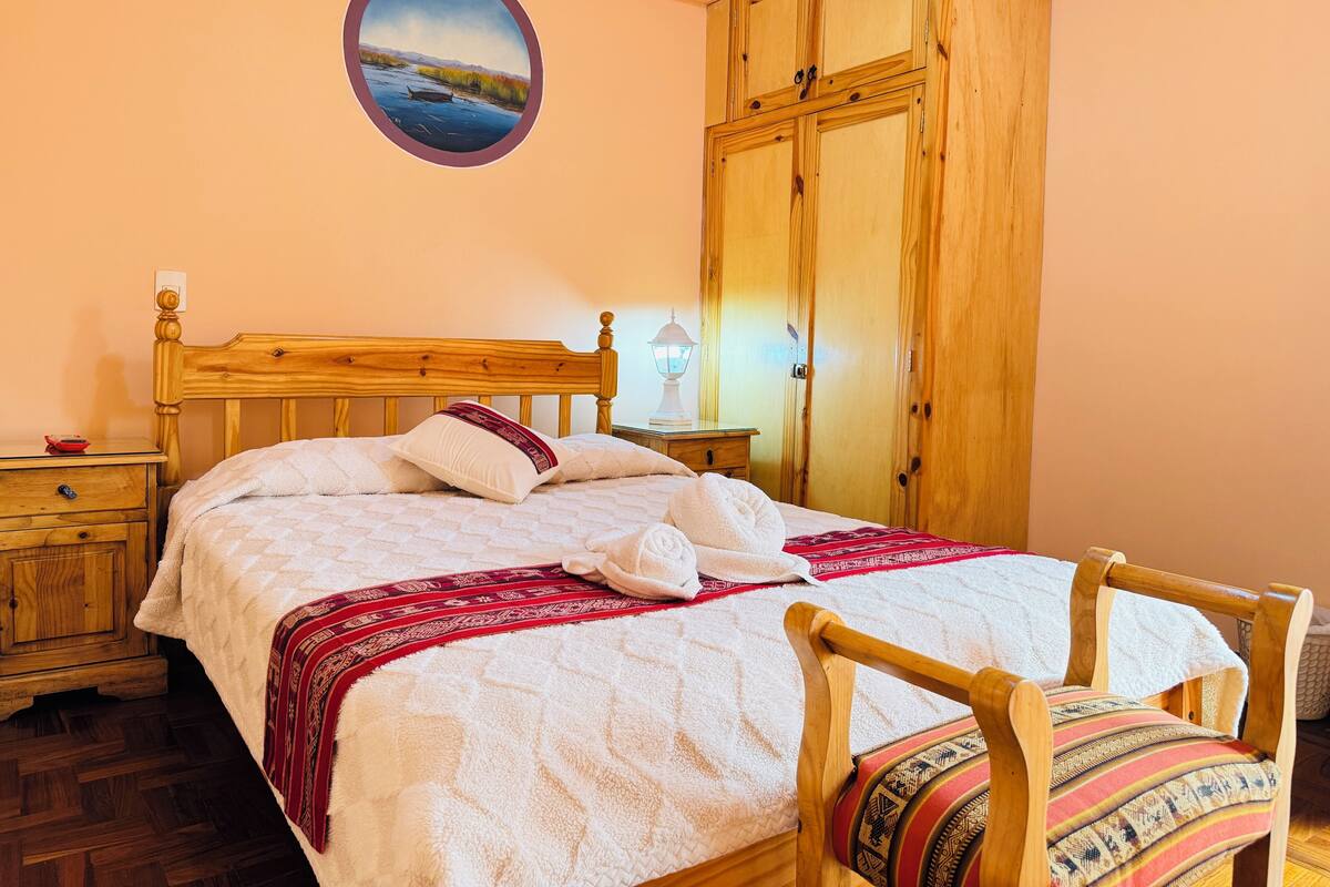 Een slaapkamer met een houten bed, nachtkastje, kast en een schilderij aan de muur.