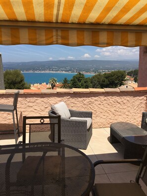 A patio with wicker furniture, a round table, and a view of a beach and cityscape.