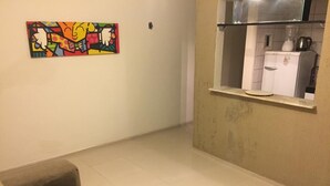 Un saló amb un sofà, un quadre abstracte i colorit, i una zona de cuina amb un frigorífic i una finestra.