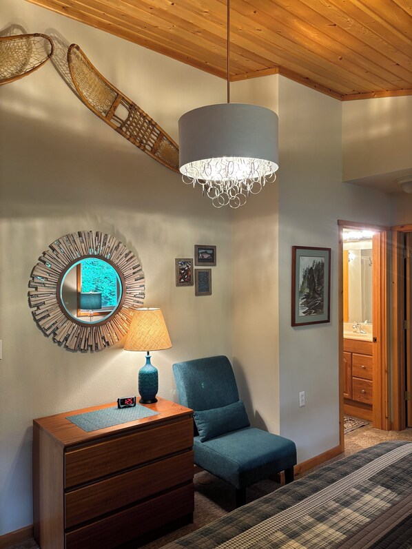 A room with a wooden ceiling, a blue chair, a wooden dresser, a wall-mounted mirror, and a chandelier. - Private lakefront home on gorgeous Kenai Lake! (Seward)