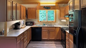 Une cuisine moderne avec des meubles en bois, un lave-vaisselle noir, une cuisinière et une fenêtre donnant sur un paysage verdoyant.