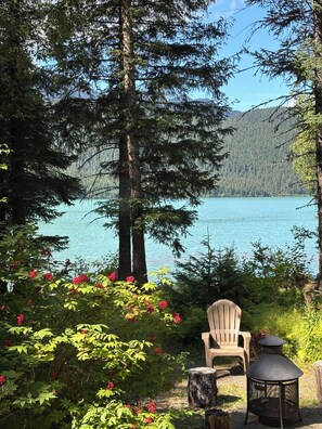 A lakeside view with a chair and a lantern, surrounded by trees and red flowers. - Private lakefront home on gorgeous Kenai Lake! (Seward)