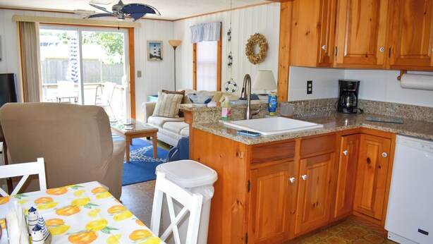 Une cuisine compacte avec des meubles en bois, un lave-vaisselle blanc et un coin repas avec une table dressée pour deux personnes.