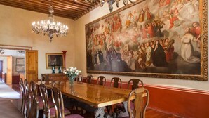 Un comedor con una larga mesa de madera, sillas ornamentadas y un gran mural en la pared.