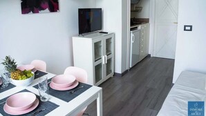 Een moderne, goed verlichte kamer met een eettafel gedekt voor twee personen, een televisie, en een keukenhoek met kastjes en een aanrecht.