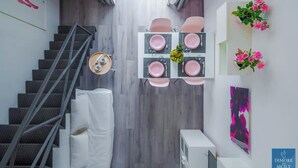 Een modern interieur met een trap, een eethoek met roze stoelen en een tafel gedekt voor vier personen, en een bloemstuk aan de wand.
