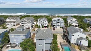 Un área residencial costera con varias casas de dos pisos, una playa al fondo y un cielo despejado.