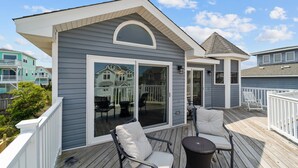 Una terraza techada con dos sillas y una mesa, un gran ventanal corredizo y una estructura anexa pequeña con techo a dos aguas.