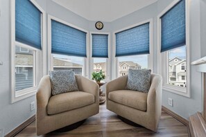 Relax in this cozy corner room with a view of neighboring houses, featuring two armchairs and a large window.