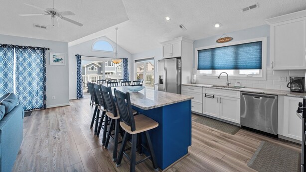 Cocina moderna con armarios blancos, una isla central con taburetes de bar, ventilador de techo y vistas al exterior.