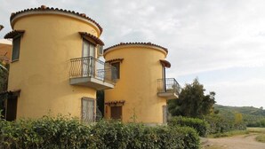 A yellow building with two balconies, surrounded by greenery and a dirt path. - Agriturismo La Petrosa - Granaio Woe (Petrosa)