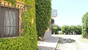 A building with a stone pathway leading to a gated entrance, surrounded by greenery and a clear sky. - Agriturismo La Petrosa - Granaio Woe (Petrosa)