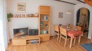 Una sala acogedora con mueble de madera para entretenimiento, una mesa de comedor con sillas y una estantería.