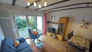 Sala de estar con sofá, sillón, mesa de centro, televisión y un comedor con mesa y sillas.