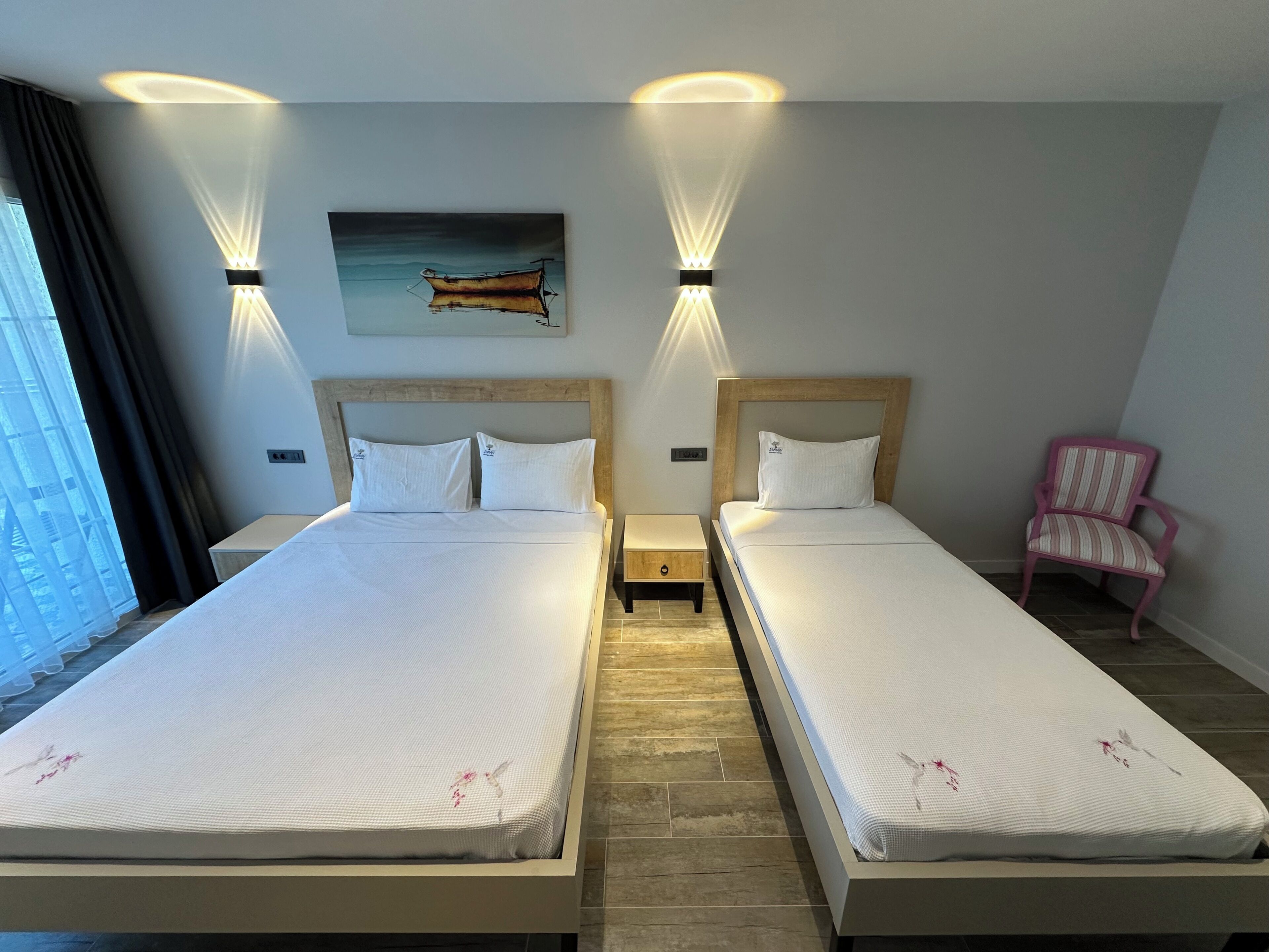 A hotel room with two beds, a painting on the wall, and a chair.