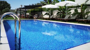 A swimming pool with a clear blue water surface, surrounded by lounge chairs and umbrellas, and a covered area with tables and chairs. - Duman Boutique Hotel (Cesme)