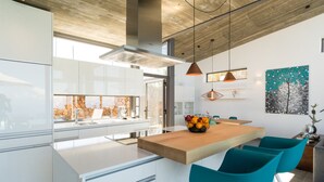 Eine moderne Küche mit einer großen Kochinsel, weißen Schränken und einer Holz Arbeitsplatte. Auf der Insel stehen zwei türkisfarbene Stühle und eine Obstschale.
