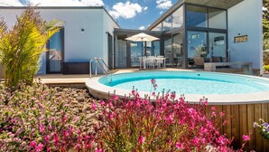 Ein modernes Haus mit Swimmingpool, Sitzgelegenheit im Freien und einem Garten mit rosa Blumen.